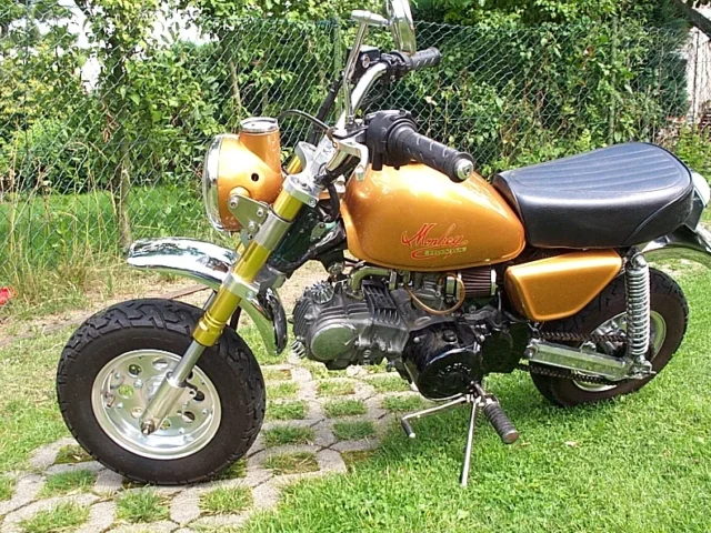 A customised Honda Monkey in gold with upside-down forks, a tuned engine and a chrome exhaust, photographed on a paved driveway.