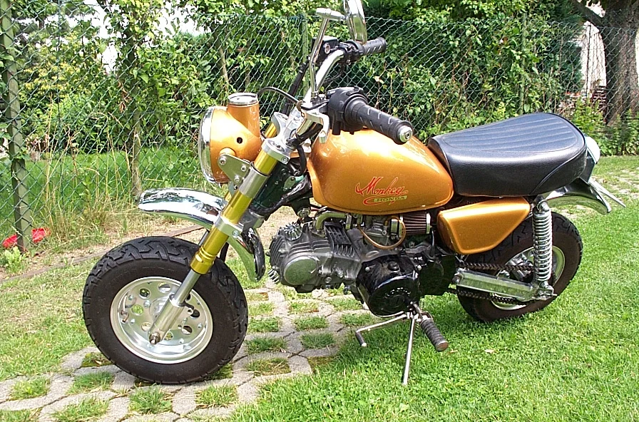 A customised Honda Monkey in gold with upside-down forks, a tuned engine and a chrome exhaust, photographed on a paved driveway.