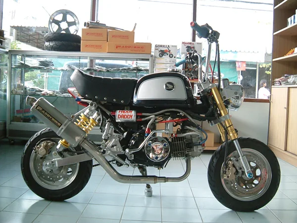 A custom Faddy Daddy mini motorcycle on the workshop floor, with parts shelving behind it.