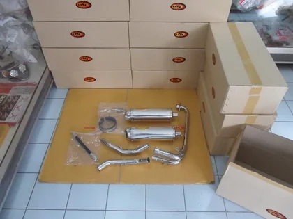 Two chrome motorcycle exhaust systems, still part-bagged, laid out on a mat in front of stacked cartons with an open carton beside them.