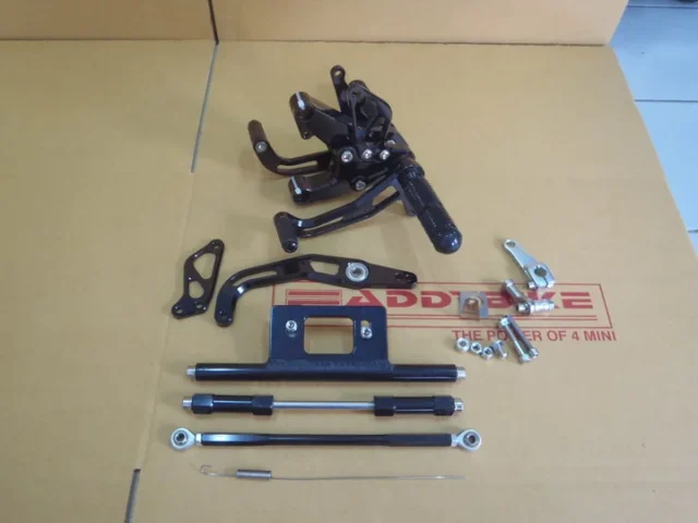 A black anodised rearset kit for the Honda Monkey laid out on a Faddybike work mat: footpeg hangers, mounting plate, linkages and connecting rods.