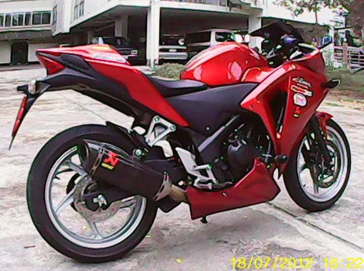 A red Honda CBR250R sports motorcycle with an aftermarket exhaust, parked on a driveway.