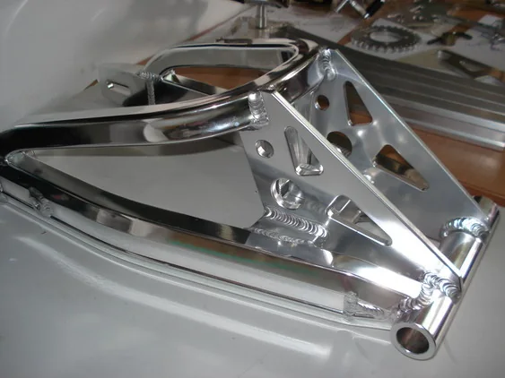A polished aluminium swingarm for the Kawasaki KSR, photographed on a workbench.