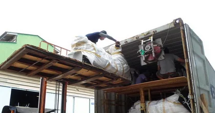 Workers lifting wrapped goods from a loading platform into a shipping container backed up to the premises.