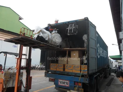 A shipping container on a truck being loaded with wrapped motorcycle parts and boxed goods at the warehouse.