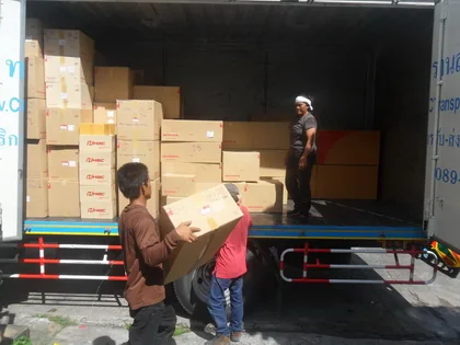Two men lifting cardboard cartons of motorcycle parts into the back of a delivery truck already stacked with boxes, ready to leave for the freight agent.