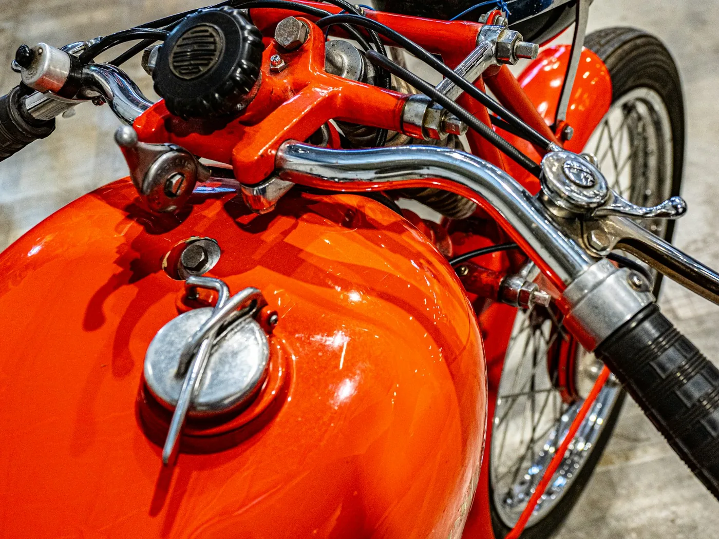 Close-up of a vintage orange motorcycle's fuel tank and handlebars