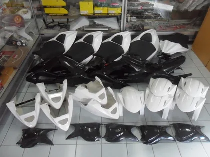 Black and white moulded motorcycle fairings and seat cowls stacked on shelving in the shop.