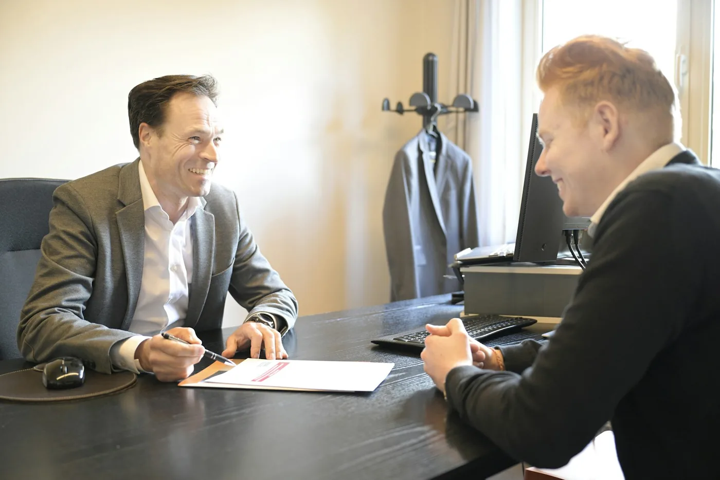 Two smiling men discussing documents at an office desk