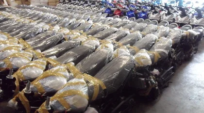 Rows of new motorcycles wrapped in plastic sheeting and strapped, lined up on the warehouse floor ready for container loading.
