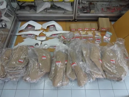 Rows of motorcycle parts wrapped in plastic and labelled, laid out on the shop floor beside white fairings and small cartons, ready to be packed.