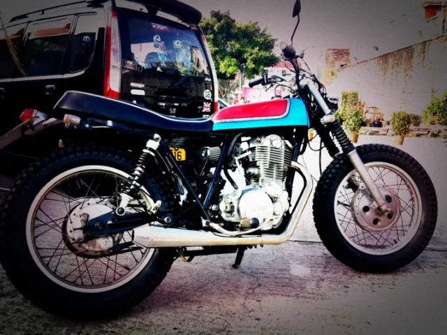 A customised Yamaha SR single-cylinder motorcycle in tracker style, with a blue and red tank, race number 66, spoked wheels and a high-level exhaust.