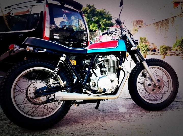 A customised Yamaha SR single-cylinder motorcycle in tracker style, with a blue and red tank, race number 66, spoked wheels and a high-level exhaust.